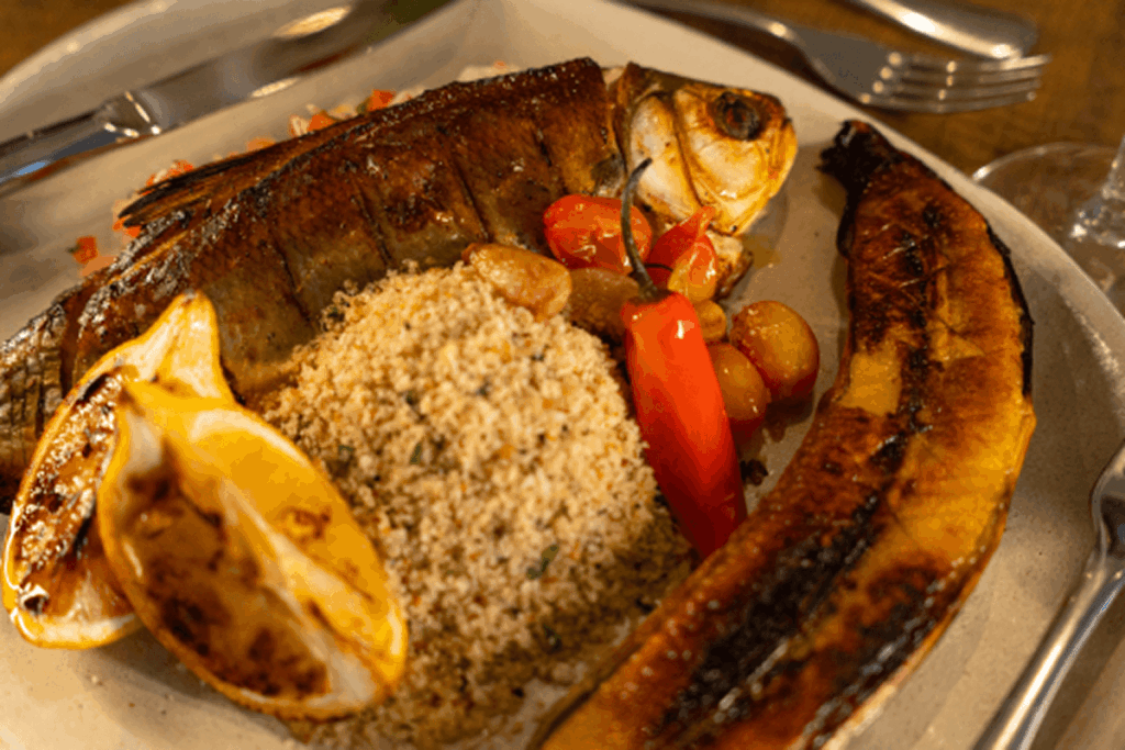 Peixe grelhado com tomates assados ​​e coentro, servido em prato claro.