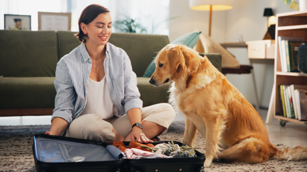 Jovem mulher, vestindo roupas casuais, prepara sua mala para viajar, acompanhada de seu cão.
