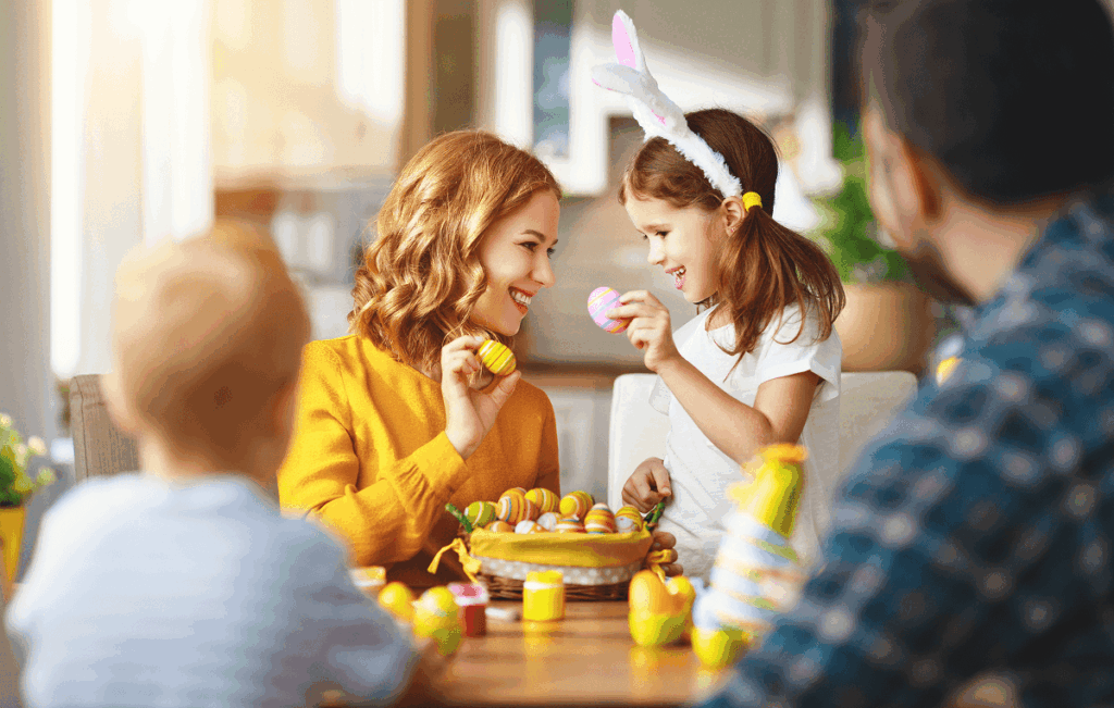Uma família caucasiana, formada por mãe, pai e filhos, pinta ovos de Páscoa para aproveitar o feriado juntos.